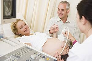 Pregnant woman getting ultrasound from doctor with husband watching