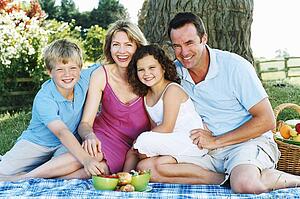 Family sitting outdoors with picnic smiling