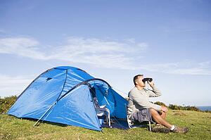 Man camping outdoors and looking through binoculars