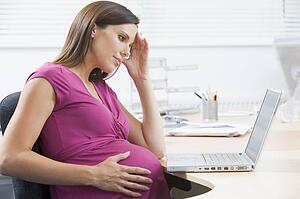 Pregnant woman at work with laptop looking stressed
