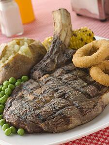 Ribeye Steak on the bone with Baked Potato Peas Onion Rings and Corn