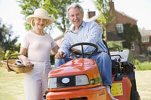 Couple outdoors with tools and lawnmower smiling