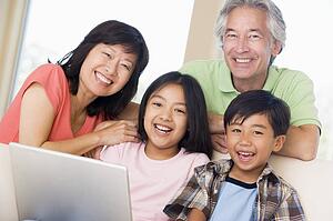 Couple with two young children in living room with laptop smiling