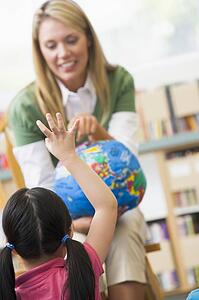 Teacher in class showing a globe with student volunteering in foreground (selective focus)