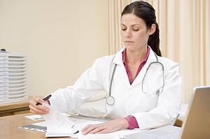 Doctor with laptop writing in doctor's office smiling