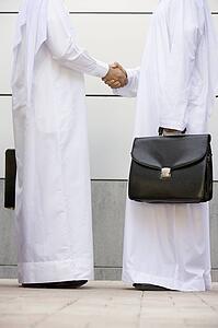 Two businessmen standing outdoors with briefcases shaking hands
