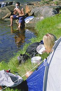 Woman outdoors at campsite with pots with man in background shaving (selective focus)