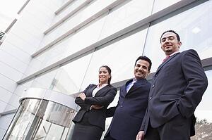 Three businesspeople standing outdoors by building smiling (high key/selective focus)
