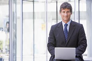 Businessman sitting in office lobby using laptop smiling