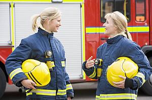 Two firewomen standing by fire engine talking