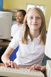 Student at computer terminal typing with student in background (selective focus)