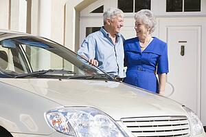 Senior couple standing with their car outside their home