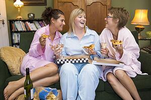 Three woman in night clothes sitting at home eating pizza