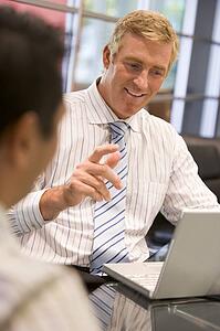 Two businessmen in boardroom with laptop talking