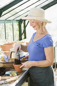 Woman in greenhouse putting soil in pot and smiling