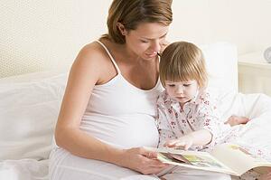Pregnant woman in bedroom reading book with daughter