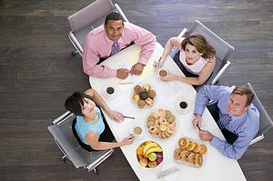 Four businesspeople at boardroom table with breakfast smiling