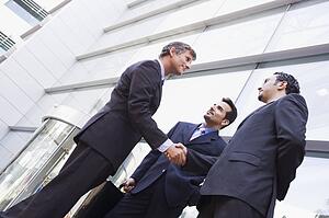 Three businessmen outdoors by building shaking hands and smiling (high key/selective focus)