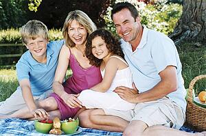 Family sitting outdoors with picnic smiling