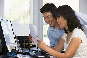 Couple in home office with computer and paperwork smiling