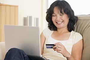 Woman in living room using laptop holding credit card and smiling