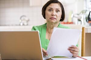 Woman in kitchen with laptop and paperwork looking worried