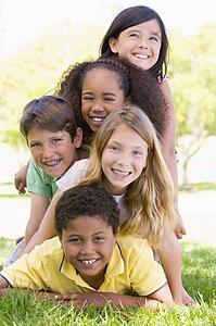 Five young friends piled up on top of each other outdoors smiling