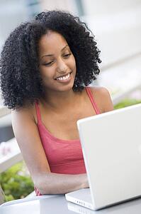 Woman sitting at table outdoors with laptop smiling (high key)