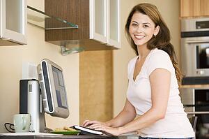 Woman in kitchen with computer smiling
