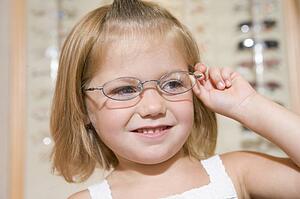 Young girl trying on eyeglasses at optometrists smiling
