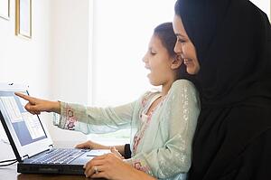Mother and daughter in office with laptop pointing and smiling (high key/selective focus) 
