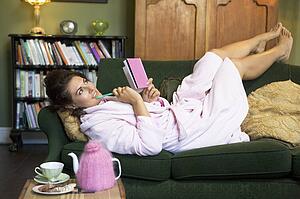 Young woman lying on sofa at home writing in her diary