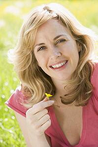 Woman sitting outdoors holding flower smiling