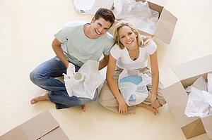 Couple sitting on floor by open boxes in new home smiling