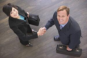 Two businesspeople indoors shaking hands smiling