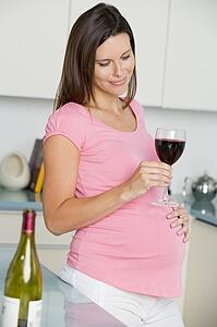 Pregnant woman in kitchen with glass of red wine smiling