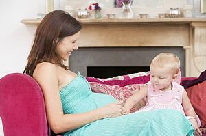 Pregnant mother with daughter in living room touching belly and smiling