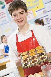 Male student holding a tray of tarts in cooking class