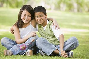 Two young children outdoors in park bonding and smiling (selective focus)