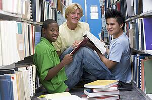Three men sitting on floor in library with books