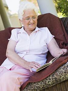 Senior woman sitting outdoors on a chair reading a book