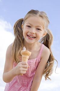 Young girl outdoors eating ice cream cone and smiling