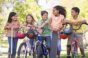 Five young friends with bicycles scooters and skateboard outdoors smiling