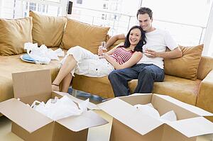 Couple relaxing with champagne by boxes in new home smiling