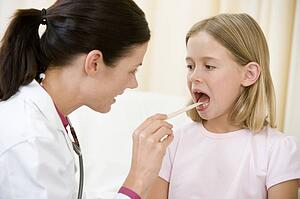 Doctor giving checkup to young girl with tongue depressor in exam room