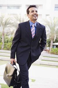 Businessman walking outdoors by building with a briefcase smiling (high key/selective focus)