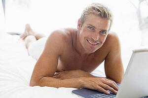 Man lying in bed with laptop smiling