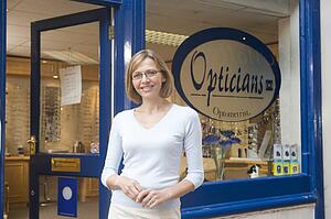 Woman standing at front entrance of optometrists smiling