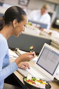 Businesswoman in cubicle with laptop eating salad