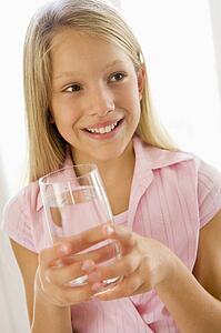 Young girl indoors drinking water smiling